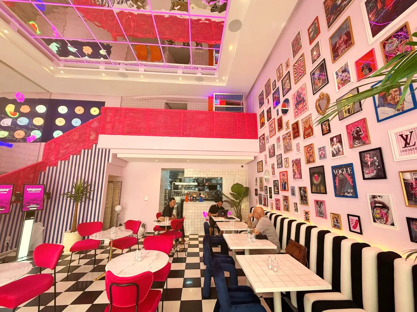 La salle de Warner : fauteuils fuchsia, sol en damier, banquette rayée et mur couvert de cadres